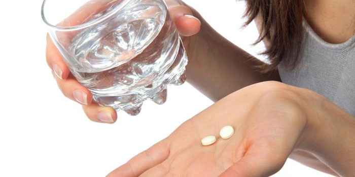 Таблетки на ладони и стакан воды в руке