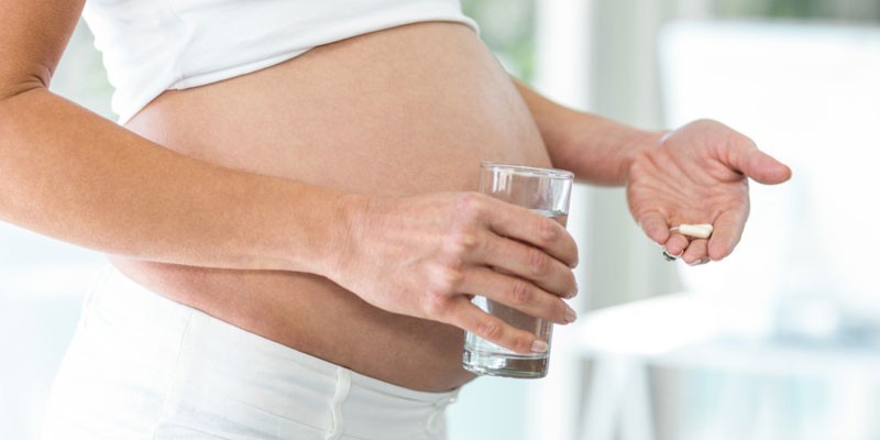 Беременная женщина с таблеткой и стаканом воды
