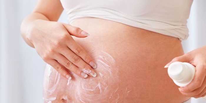 Беременная женщина смазывает кожу живота кремом