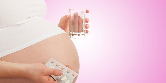 Беременная с таблетками и стаканом воды в руках