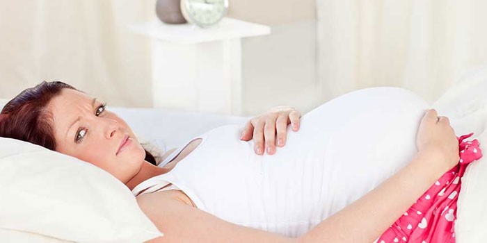 Беременная девушка лежит в постели