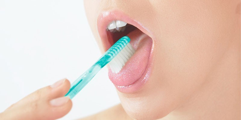 Девушка чистит язык зубной щеткой