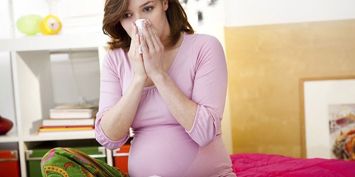 Беременная женщина вытирает нос платком