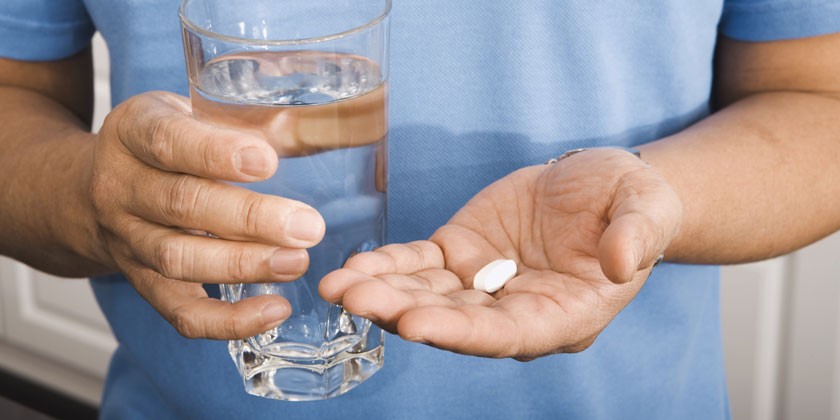 Мужчина с таблеткой и стаканом воды в руках