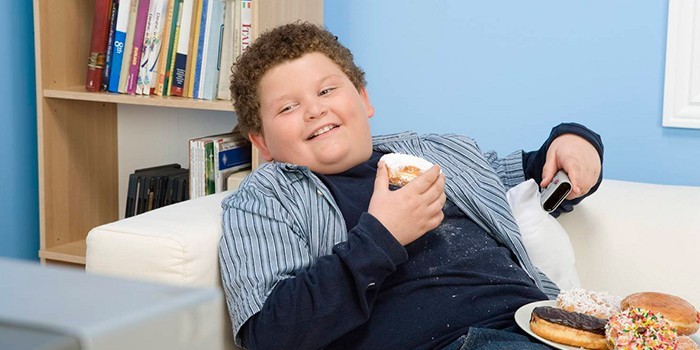 Мальчик лежит на диване и ест пончики